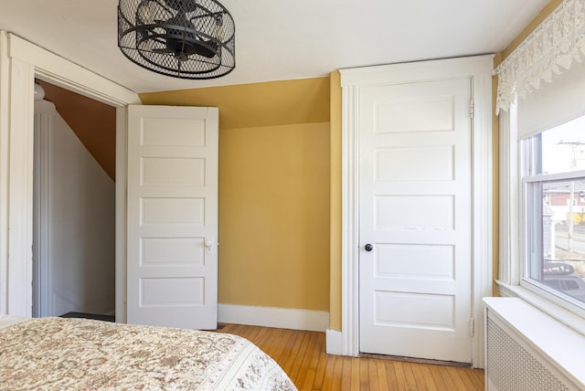 bedroom featuring light wood-type flooring, radiator heating unit, and baseboards