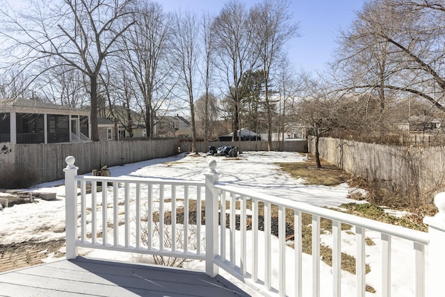 snow covered deck featuring a fenced backyard and a sunroom