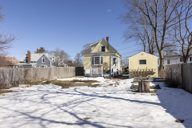 snow covered back of property featuring a chimney, fence private yard, and an outbuilding