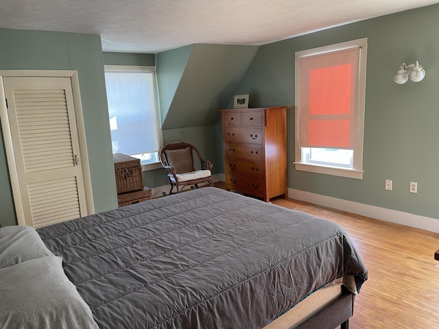 bedroom featuring multiple windows, vaulted ceiling, baseboards, and wood finished floors