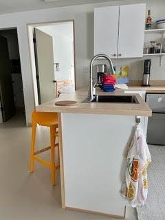 kitchen featuring open shelves, a peninsula, a sink, light countertops, and white cabinetry