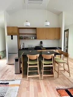 kitchen featuring high vaulted ceiling, open shelves, a kitchen breakfast bar, freestanding refrigerator, and light wood-style floors