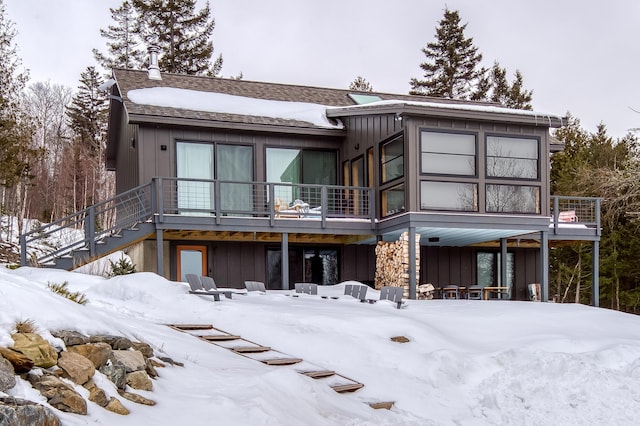 snow covered rear of property featuring stairs and board and batten siding