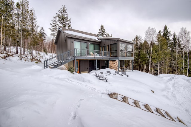 snow covered property with stairs, a garage, and a sunroom