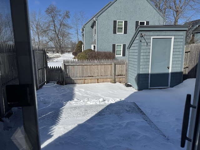 snow covered rear of property featuring fence private yard, a storage unit, and an outdoor structure