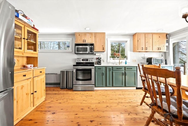 kitchen with light wood finished floors, glass insert cabinets, light countertops, stainless steel appliances, and green cabinetry