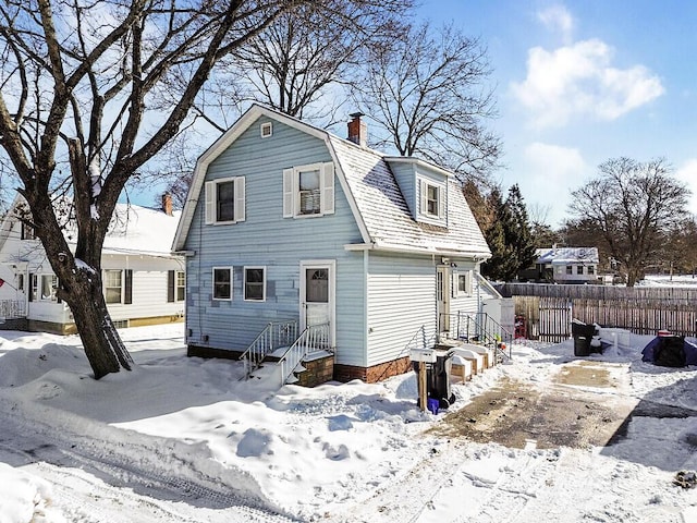 view of front of property with fence, a chimney, and a gambrel roof