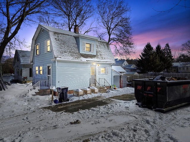 snow covered back of property with a chimney, fence, and a gambrel roof