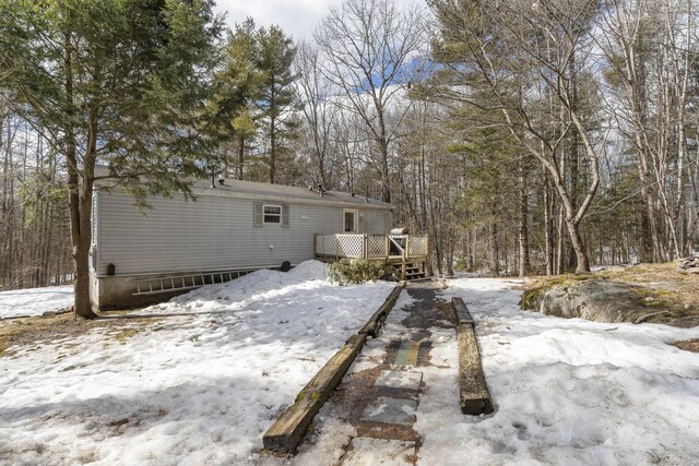 snow covered house featuring a wooded view and a deck