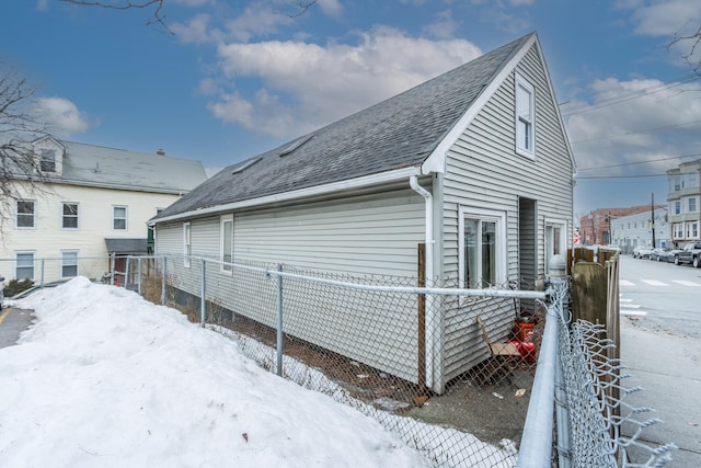 view of snow covered exterior featuring roof with shingles and fence