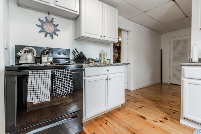 kitchen with a paneled ceiling, light wood-style floors, black / electric stove, and white cabinets