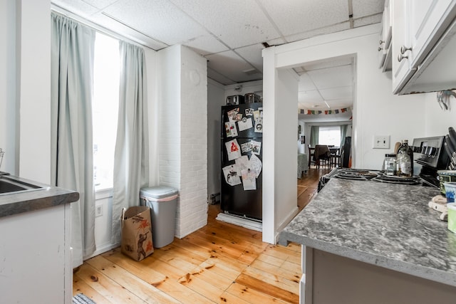 kitchen featuring a paneled ceiling, light wood finished floors, white cabinets, and freestanding refrigerator