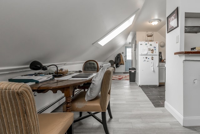 dining room with vaulted ceiling with skylight, wood finish floors, a baseboard radiator, and baseboards