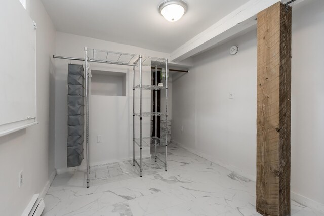 basement with a baseboard heating unit, marble finish floor, and baseboards