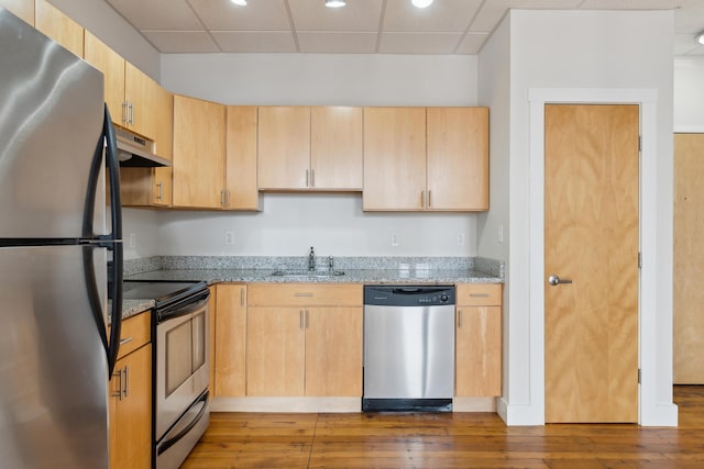 kitchen with hardwood / wood-style flooring, under cabinet range hood, a sink, appliances with stainless steel finishes, and light stone countertops