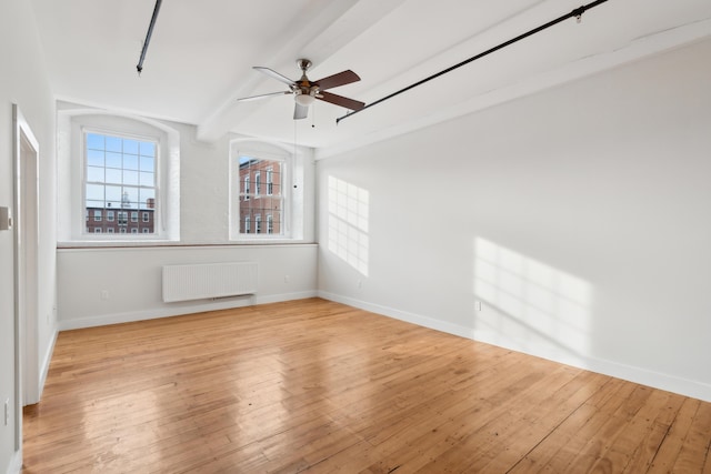 unfurnished room featuring radiator, light wood-type flooring, baseboards, and beam ceiling