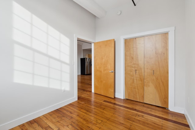 unfurnished bedroom featuring light wood-style floors, baseboards, beam ceiling, and freestanding refrigerator