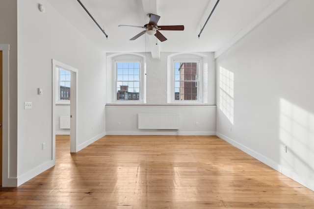 empty room with a ceiling fan, radiator heating unit, a wealth of natural light, and light wood-style floors