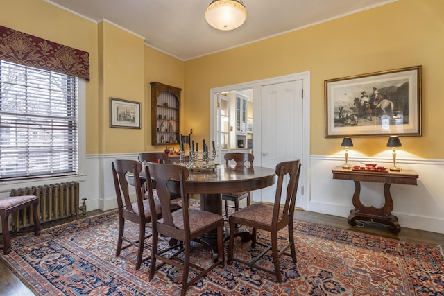 dining room with ornamental molding, a wainscoted wall, radiator, and wood finished floors