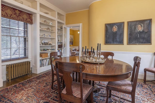 dining space featuring radiator heating unit, crown molding, built in shelves, and wood finished floors
