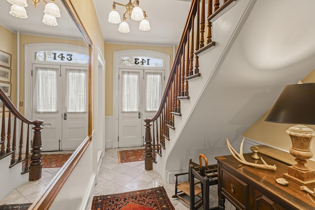 foyer entrance featuring light tile patterned flooring, a wainscoted wall, a notable chandelier, crown molding, and stairway