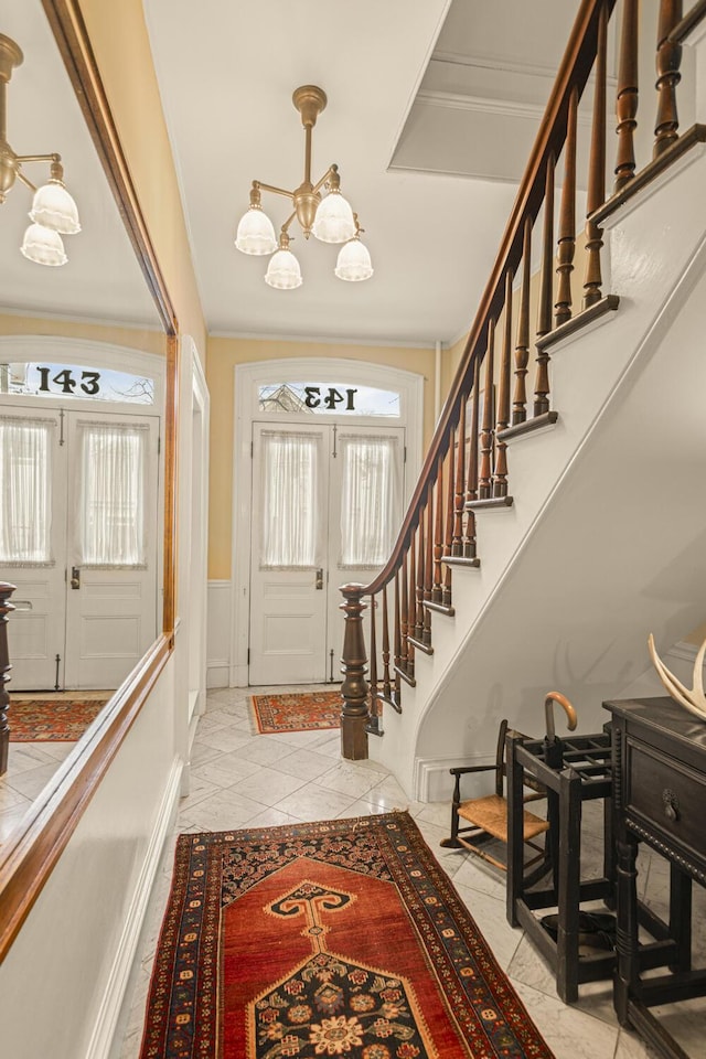 entrance foyer with a wainscoted wall, crown molding, stairway, and a chandelier