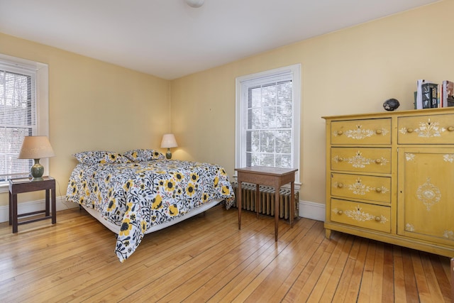 bedroom featuring baseboards, radiator heating unit, and light wood-style floors