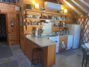 kitchen featuring lofted ceiling, concrete flooring, a peninsula, freestanding refrigerator, and open shelves