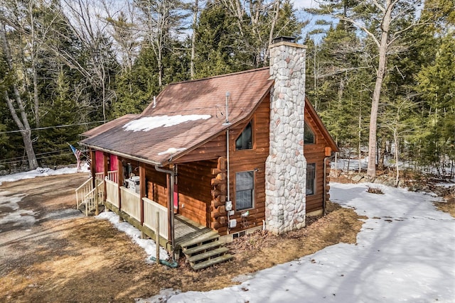 view of front of home with a porch, log exterior, roof with shingles, and a chimney