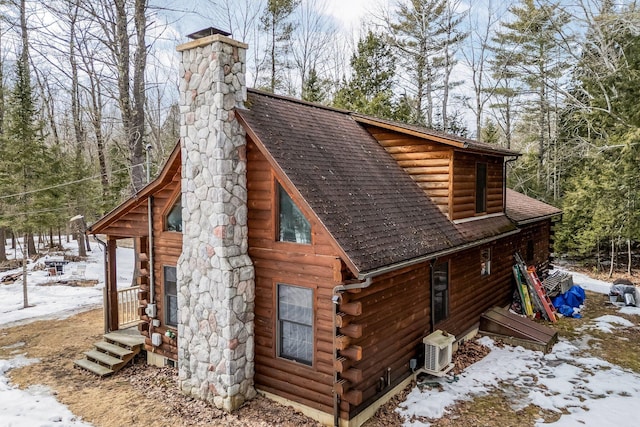 exterior space with a chimney, ac unit, a shingled roof, and log siding