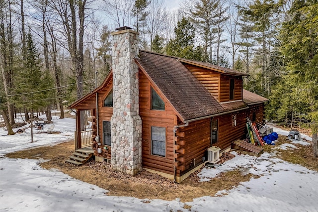 snow covered property with a garage, log exterior, a chimney, and roof with shingles