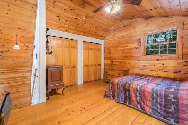 bedroom featuring multiple closets, hardwood / wood-style flooring, wooden walls, lofted ceiling, and wood ceiling