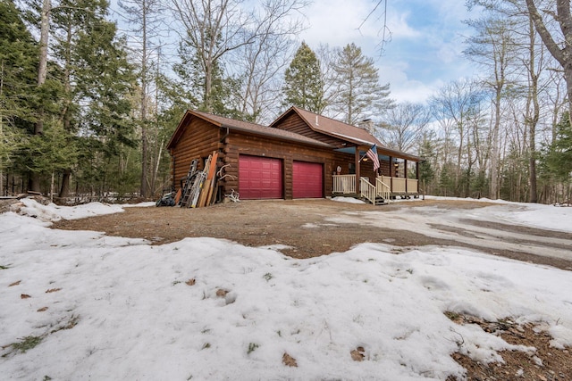 view of snowy exterior featuring log exterior, a chimney, and a garage