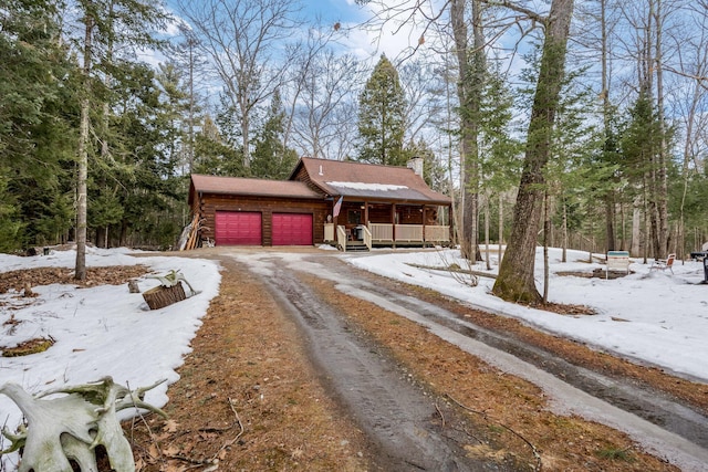 chalet / cabin featuring driveway, a porch, an attached garage, log siding, and a chimney