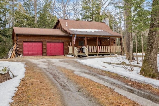 view of front facade with log siding, covered porch, a chimney, a garage, and driveway