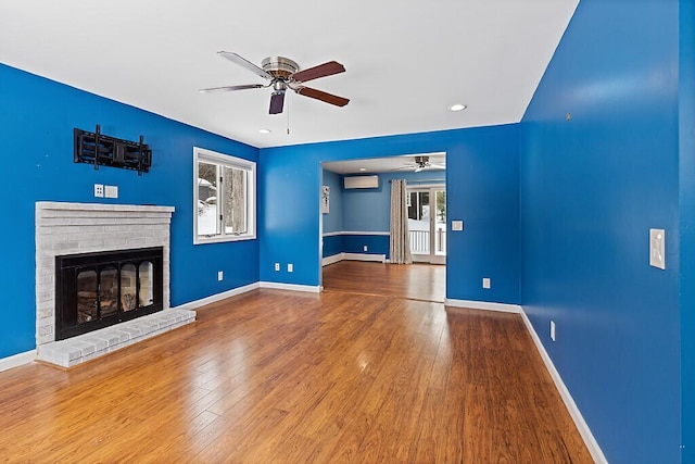 unfurnished living room with a ceiling fan, a brick fireplace, wood-type flooring, and baseboards