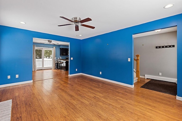 empty room featuring a baseboard radiator, baseboards, and wood finished floors