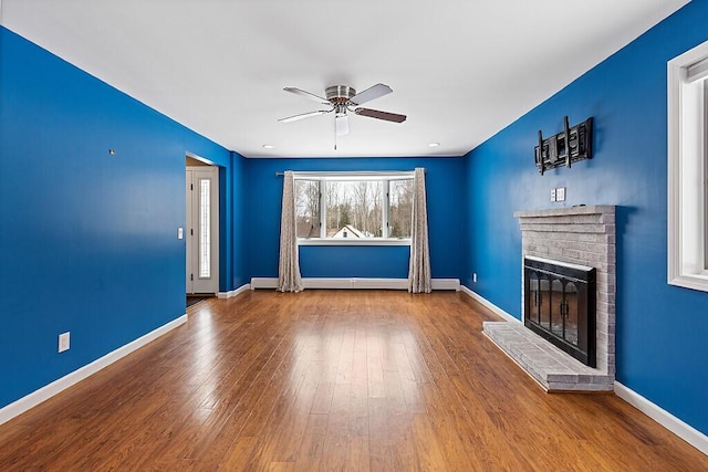 unfurnished living room with a brick fireplace, a ceiling fan, baseboards, and hardwood / wood-style floors