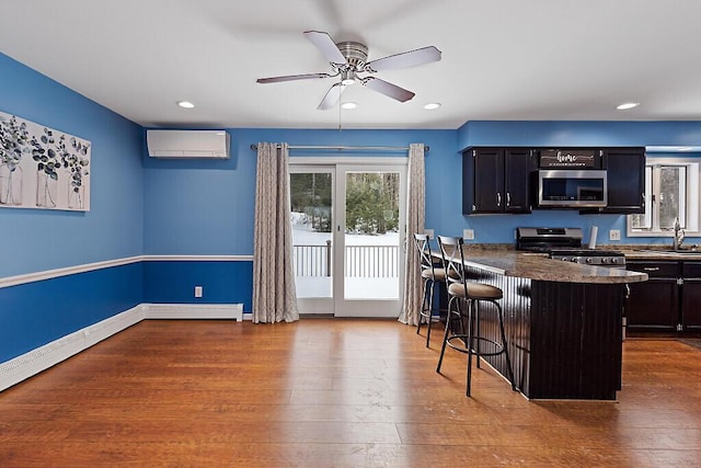 kitchen featuring a breakfast bar area, appliances with stainless steel finishes, a sink, wood finished floors, and a wall mounted air conditioner