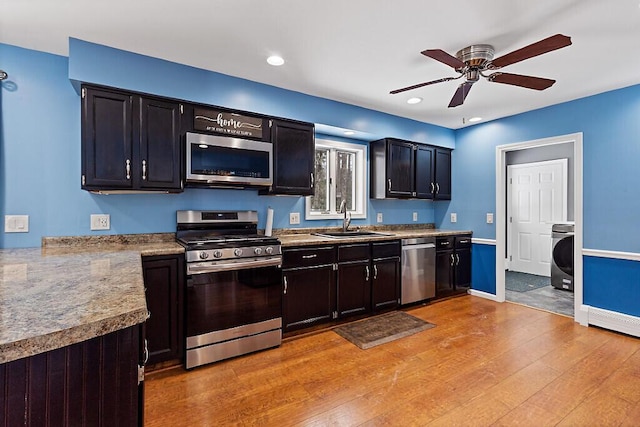 kitchen with light wood finished floors, baseboards, appliances with stainless steel finishes, washer / clothes dryer, and a sink