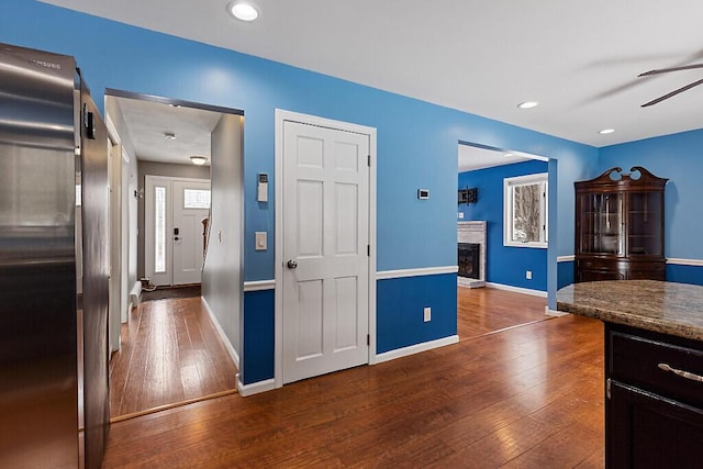 kitchen with a fireplace with raised hearth, dark wood finished floors, baseboards, and ceiling fan