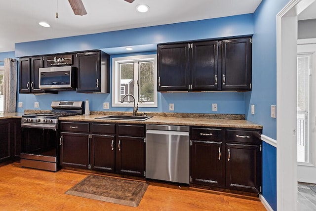 kitchen featuring stainless steel appliances, light wood-style floors, a ceiling fan, a sink, and baseboards