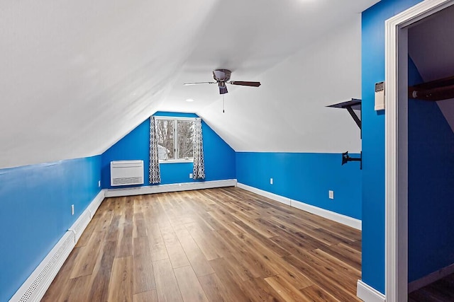 additional living space with a wall unit AC, a baseboard radiator, baseboards, and wood finished floors