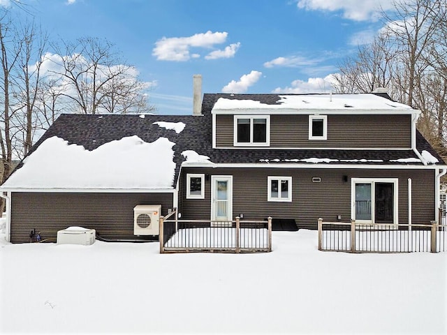 snow covered back of property with a shingled roof and a chimney