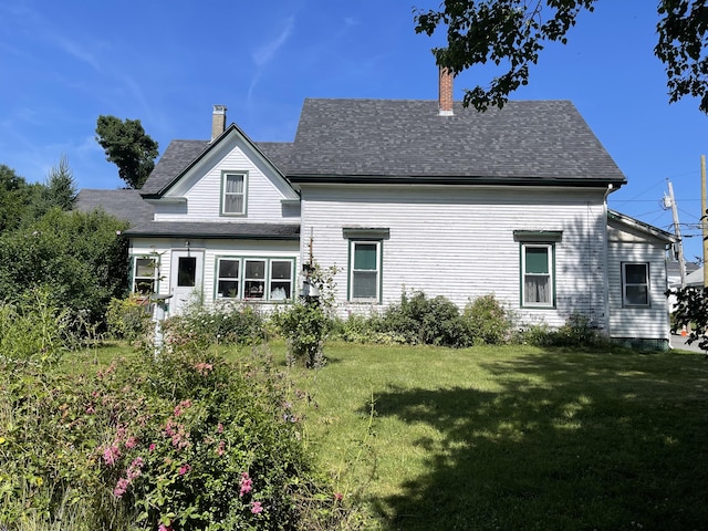 back of house with a lawn, roof with shingles, and a chimney