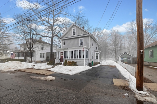 american foursquare style home featuring aphalt driveway, a chimney, an outdoor structure, and a sunroom