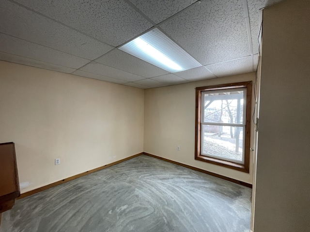 empty room featuring concrete flooring, a drop ceiling, and baseboards