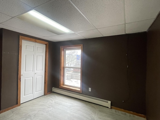 unfurnished bedroom featuring baseboard heating and a drop ceiling