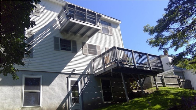 rear view of property with a deck, a lawn, and stucco siding