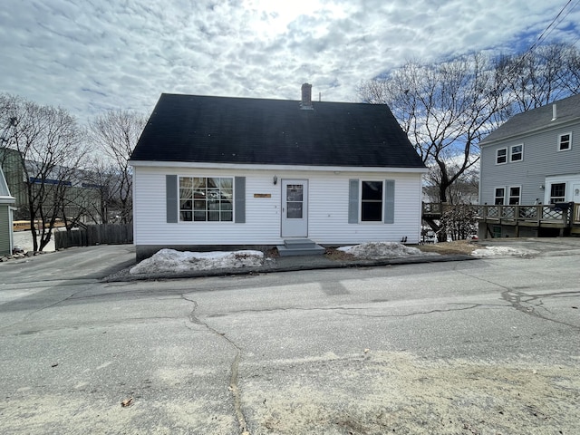 view of front of home featuring entry steps, a chimney, a deck, and roof with shingles